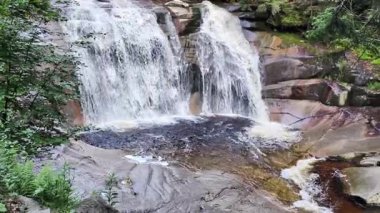Kayalar ve yeşilliklerle çevrili gür bir ormanda sakin bir şelale keşfet. Bu huzurlu vaha rahatlamaya davet eder ve doğanın güzelliğini yakalar.