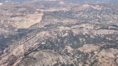 Göz kamaştırıcı bir hava manzarası parlak, berrak bir gökyüzünün altında engebeli dağlar ve kayalık araziler sergiliyor.