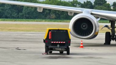 Bir yer destek aracı şu anda havaalanının yoğun pistinde bir uçak motoruna hizmet veriyor.