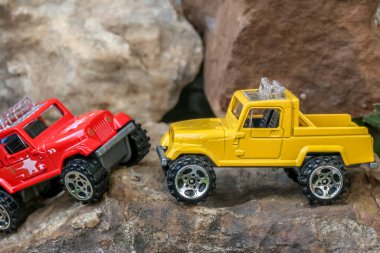 Küçük sarı bir 4x4 kamyonetin minyatür bir görüntüsü engebeli kayalık bir yolda, küçük bir uçurumun kenarında duruyor. Maceralı ve zorlu bir yolculuğun yaratıcı, eğlenceli bir temsili..