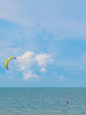 Tayland 'da Hua Hin plajında zümrüt dalgalarda sörf yapan yalnız bir uçurtma sörfçüsünün dikey görüntüsü. Güneydoğu Asya 'da açık mavi gökyüzü ve kabarık bulutlarla yaz manzarası.