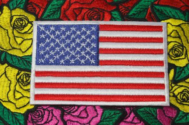 Amerika 'nın gururu, sürdürülebilirliği ve kültürel zanaatkarlığını yansıtan, iplik ve kumaştan yapılmış renkli el yapımı gül nakışlarına odaklanmış, eko dostu Amerikan bayrağının yatay görüntüsü.