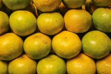 Taze Tayland bal mandalinalarının yatay yakın plan çekimi dokulu sarı kabuk ile yeşil, tatlı keskin tadı karıştırılmış yerel sokak meyveleri düzenli bir sıra halinde dizilmiş.