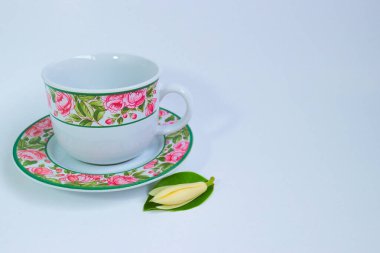 Beyaz bir şampa çiçeği ve yeşil yaprakla eşleştirilmiş, gül desenleriyle süslenmiş, retro tarzı bir seramik fincan ve uyumlu bir fincan tabağı. Saf beyaz stüdyo arkaplanı ve sağında fotokopi alanı olacak şekilde ayarla. Kültürel, yaşam tarzı ve çay temalı içerik için mükemmel.