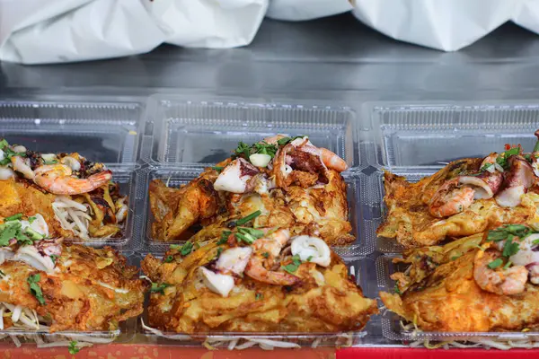 Lezzetli Tayland istiridye omleti (Hoy Tod) karides, kalamar, fasulye filizi ve bitkilerle kaplı şeffaf plastik bir kabın içinde servis edilir. Tayland 'da gece marketlerinde ve gıda tezgahlarında bulunan favori sokak yemekleri..