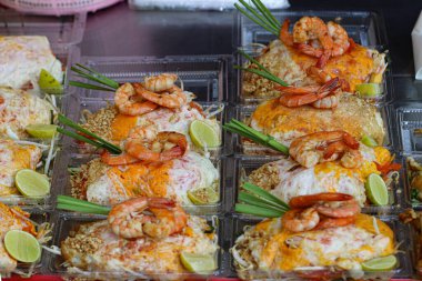 Tayland Pad Tayland karidesi yumurtaya sarılmış, limon, fıstık, lahana ve soğanlı şeffaf plastik bir kabın içinde servis ediliyor. Tayland 'ın ünlü sokak yemekleri kültürünü gözler önüne seren renkli bir yemek..