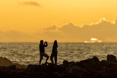 Gün batımında bir kadının fotoğrafını çeken bir adamın silüeti. İki kişi. bulutlu manzara.