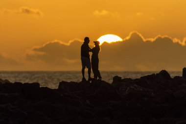 Gün batımında birbirine bakan bir çiftin silueti. Bulutlu arazi.