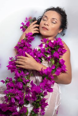 Genç Latin kadın mor çiçekler ve sütle banyo yapıyor..