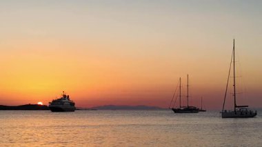 Alacakaranlıkta sakin bir deniz manzarası. Güneş ufuktan batıyor, sıcak bir altın parıltı saçıyor. Bir yolcu gemisi ve yelkenliler durgun okyanus suyunda yüzen renkli gökyüzüne karşı siluetlenir. Özgürlük, Aşk, Macera, Huzur, Seyahat Konsepti.