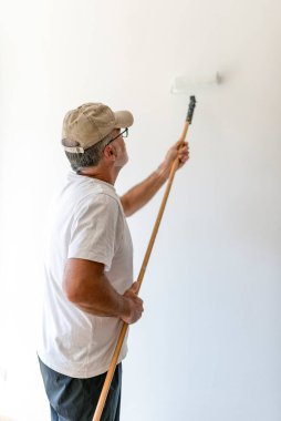 Üst düzey boyacı, teleskopik sapına kolayca ulaşabilmek için boya silindiri kullanarak duvara taze beyaz boya sürüyor.