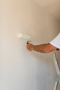 Bir boyacının elini boya silindiri ile kapatıyoruz. Duvara yeni bir kat beyaz boya sürüyoruz.