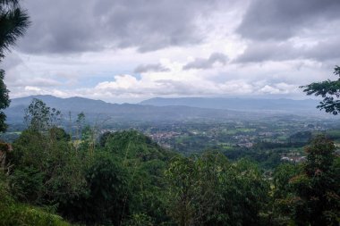 Dağılmış köyleri ve uzak dağları ile panoramik bir manzara dramatik bulutlu gökyüzü altında, yüksek bir orman yamacından yakalandı.