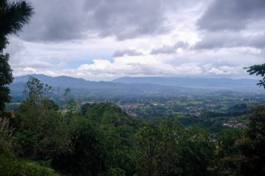 Dağılmış köyleri ve uzak dağları ile panoramik bir manzara dramatik bulutlu gökyüzü altında, yüksek bir orman yamacından yakalandı.