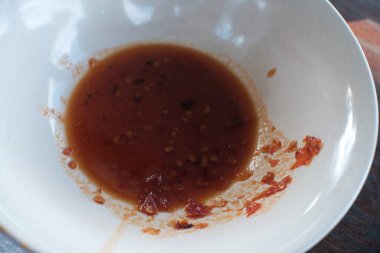 İçinde az miktarda baharatlı kırmızı biber sosu bulunan beyaz bir kaseye yakın plan çekimde görülebilir tohumlar ve yağ kalıntıları yakın zamanda bitirilmiş bir yemeği işaret ediyor..