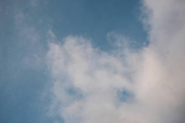 Dağılmış beyaz bulutlar parlak mavi bir gökyüzünde sürükleniyor, açık ve havadar bir atmosfer yaratıyor, gün ışığında düşük bir açıyla çekiliyor..