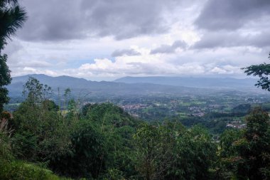 Dağılmış köyleri ve uzak dağları ile panoramik bir manzara dramatik bulutlu gökyüzü altında, yüksek bir orman yamacından yakalandı.