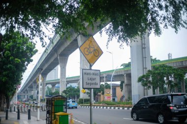 Yoğun bir şehir yolu yakınında, arka planda yüksek tren rayları ve modern altyapısı bulunan bir bisiklet şeridi (