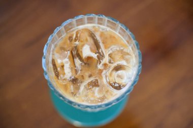 Sütlü ferahlatıcı buzlu kahvenin tepeden tırnağa görüntüsü. Krema ve dondurma sergileniyor. İçki, ahşap bir masanın üzerinde yeşil bir bardak üzerinde, kaburgalı bir bardakta servis edilir..