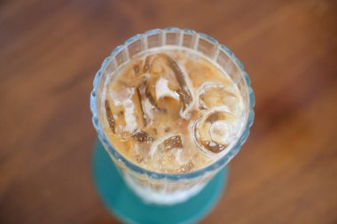 Sütlü ferahlatıcı buzlu kahvenin tepeden tırnağa görüntüsü. Krema ve dondurma sergileniyor. İçki, ahşap bir masanın üzerinde yeşil bir bardak üzerinde, kaburgalı bir bardakta servis edilir..