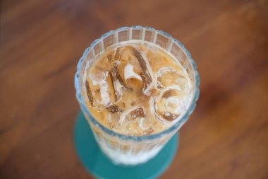 Sütlü ferahlatıcı buzlu kahvenin tepeden tırnağa görüntüsü. Krema ve dondurma sergileniyor. İçki, ahşap bir masanın üzerinde yeşil bir bardak üzerinde, kaburgalı bir bardakta servis edilir..