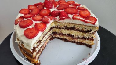 Beyaz ve kırmızı çilekli bir kekin dikey görüntüsü. Beyaz ve çikolata katmanlı kek ve dilimlenmiş çilek ve siyah masanın üzerinde beyaz krema.. 