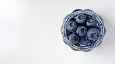 Yaz meyvelerini yaban mersinli cam mavi vazoya koy. Beyaz arka planda böğürtlen vazosu.