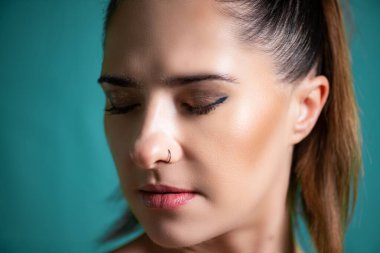 Sakin bir ifadeye ve kapalı gözlere sahip güzel bir genç kadın canlı bir deniz mavisi arkaplanına yakalanıyor. Saçları parlak at kuyruğu şeklinde ve sakin, yansıtıcı bir tavır sergiliyor..