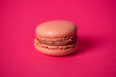 Fındık dolgulu bir badem kurabiyesi yakın planda gösterilir. Makaron beyaz bir zemin üzerinde izole edilir, bu da canlı kırmızı rengini ve dokulu yüzeyini vurgular..