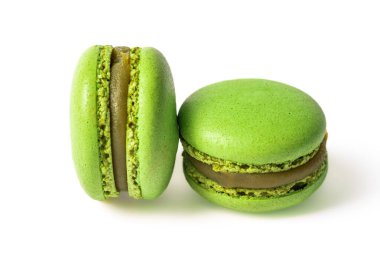 Beyaz arka planda kremalı şam fıstıklı iki yeşil badem kurabiyesi var. Makaronlar biraz bulanık, yumuşak ve ruhani bir etki yaratıyor. Görüntü, bu popüler Fransız babalarının narin güzelliklerini ve karmaşık detaylarını yansıtıyor.