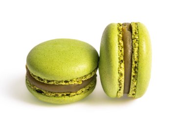 Beyaz arka planda kremalı şam fıstıklı iki yeşil badem kurabiyesi var. Makaronlar biraz bulanık, yumuşak ve ruhani bir etki yaratıyor. Görüntü, bu popüler Fransız babalarının narin güzelliklerini ve karmaşık detaylarını yansıtıyor.