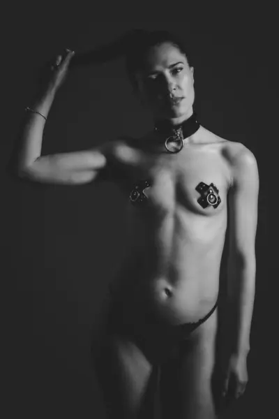 Kendinden emin bir kadın, tasması ve minimalist siyah kıyafeti olan loş bir stüdyoda poz veriyor. Cesur ve güçlü bir duruş sergilemek. Baştan çıkarıcı rol yapan seksi boğucu kadın. Bdsm konsepti.