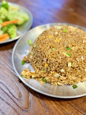 Kızarmış pirinç, metal bir tabakta ve kızarmış sebzelerle servis edilir.