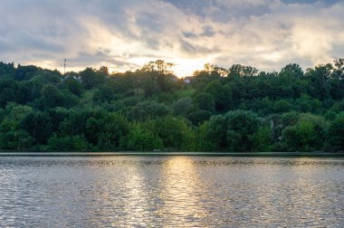 Gün batımında, ormanın yamacını yansıtan sakin bir göl ve huzurlu bir ahenkle dağılmış tepe evleri..
