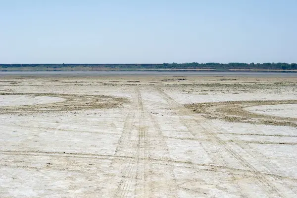 Açık mavi gökyüzünün altında, kuru ve çorak bir arazide lastik izleri uzanıyor. Issız bir arazide insan varlığını işaret ediyor..