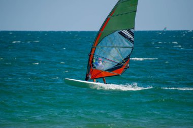 Rüzgâr sörfçüsü dalgalı okyanus dalgalarını hızlı bir şekilde geçiyor. Canlı yeşil, turuncu ve mavi yelkenli ile. Rüzgarlı, güneşli bir günde..