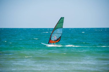 Rüzgâr sörfçüsü dalgalı okyanus dalgalarını hızlı bir şekilde geçiyor. Canlı yeşil, turuncu ve mavi yelkenli ile. Rüzgarlı, güneşli bir günde..