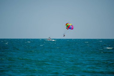  Bulgaristan 'da açık ve güneşli bir günde, canlı renkli bir paraşütün altında turkuaz okyanus dalgaları üzerinde süzülüyor