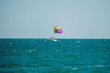  Bulgaristan 'da açık ve güneşli bir günde, canlı renkli bir paraşütün altında turkuaz okyanus dalgaları üzerinde süzülüyor