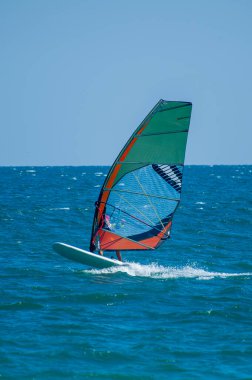 Bulgaristan 'da rüzgarlı, güneşli bir günde dalgalı okyanus dalgalarını canlı yeşil, turuncu ve mavi yelkenliyle geçen bir rüzgar sörfçüsü
