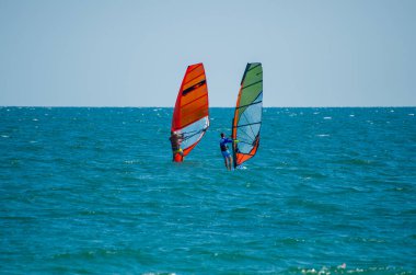 Bulgaristan 'da açık ve güneşli bir gökyüzünün altında iki rüzgar sörfçüsü ışıl ışıl mavi denizde yarışıyor