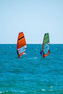 Bulgaristan 'da açık ve güneşli bir gökyüzünün altında iki rüzgar sörfçüsü ışıl ışıl mavi denizde yarışıyor