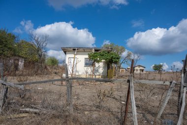Sarmaşıkla kaplı girişi olan küçük, yıpranmış bir ev, kırsal alanda kırık bir çitin arkasında sessizce duruyor..