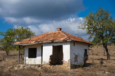  Terk edilmiş, kırmızı kiremitli çatılı beyaz bir ev kurak, ıssız bir avluda duruyor karamsar, bulutlu bir gökyüzünün altında..