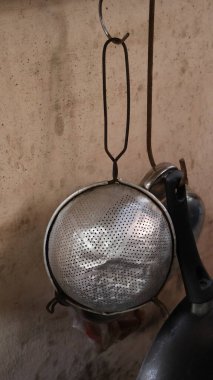 Paslanmaz çelik bir kevgir duvarların yağ lekeleriyle dolu olduğu eski bir mutfakta asılı duruyor.