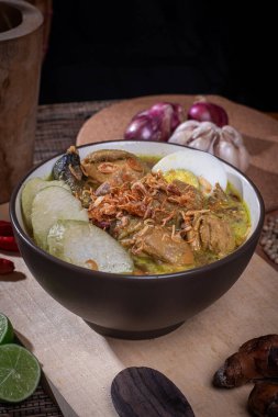 Bir kase Endonezya Opor Ayam 'ı haşlanmış yumurta, longa ve taze otlarla çevrili ahşap bir tahtada servis edilen kavrulmuş arpacık soğanları ile..