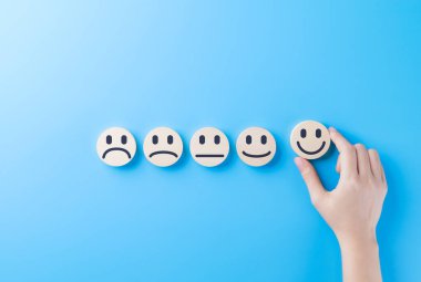 Müşteri memnuniyeti geri bildirimi ve değerlendirme konsepti. Geri bildirim anketi ve gözden geçirme için mavi arkaplanda farklı tatmin seviyelerini temsil eden gülen yüz simgesi dizisinden elle seçiliyor.