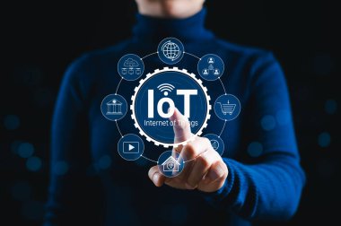 Nesnelerin İnterneti (IoT) Teknoloji Konsepti. Bir kişi, akıllı aygıtları, bağlantıyı ve endüstriler arasında çeşitli uygulamaları temsil eden simgelerle parlayan IoT arayüzüne dokunur..