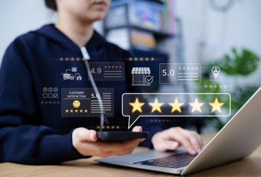 Müşteri değerlendirmesi ve memnuniyet geri bildirimi konsepti. Beş yıldızlı telefon ve dizüstü bilgisayar kullanan kişi, değerlendirme puanları, çevrimiçi geri bildirim, yorumlar, müşteri analitiği temsil eden tatmin simgeleri,