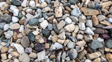 Beyaz, gri, kahverengi ve mavi-yeşil gibi çeşitli renklerde pürüzsüz, doğal olarak yuvarlak taşların bir karışımını gösteren, nehir taşlarının tam kare kare görüntüsü.